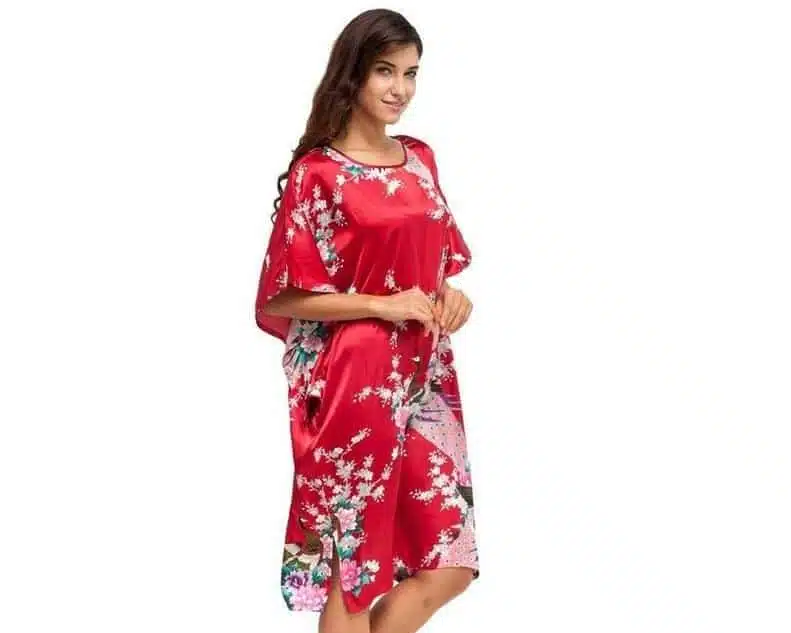 Jeune femme brune , se tient debout légèrement en biais, porte une chemise de nuit style chine de couleur rouge avec des motifs floraux, elle est présentée sur fond blanc